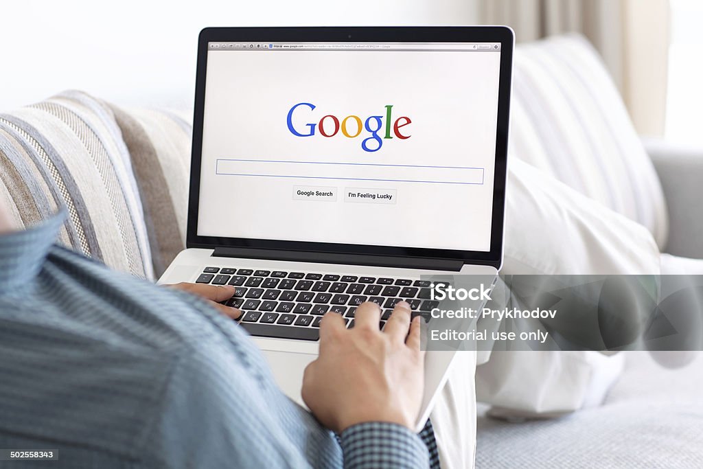 man sitting the MacBook retina with site Google on screen Simferopol, Russia - July 9, 2014: Google biggest Internet search engine. Google.com domain was registered September 15, 1997. Google - Brand-name Stock Photo