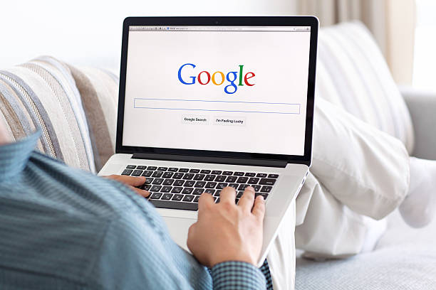 człowiek siedzi w siatkówce macbook z witryny google na ekranie - google zdjęcia i obrazy z banku zdjęć