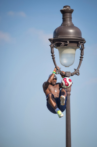 Paris, France - May 15, 2014: Soccer player makes a soccer freestyle demonstration attach in a light pole in front of Sacre Coeur church.