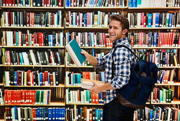istock Smiling student holding books in library 502575934
