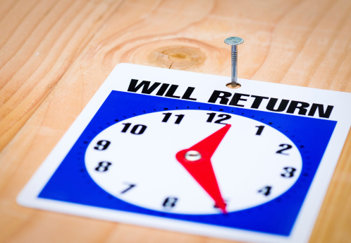 Close up on will return sign nailed to a wood background including return time clock – shallow DoF
