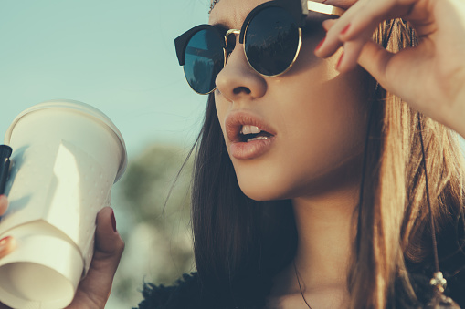 Pretty hipster girl in sunglasses with cup of coffee. Close-up lifestyle outdoor portrait