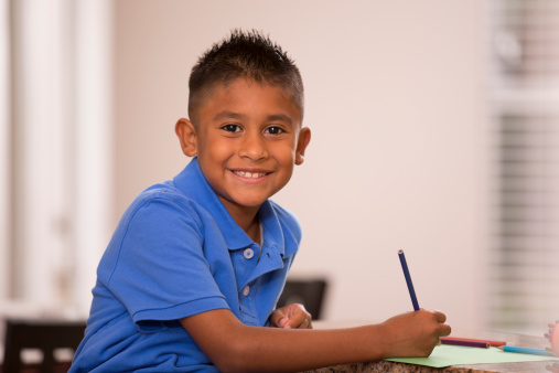 Cute, Hispanic child does homework in home kitchen.  Colored pencils.