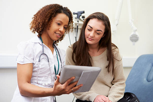 Nurse Showing Patient Test Results On Digital Tablet Nurse Showing Patient Test Results On Digital Tablet In Clinic Sitting Down woman talking to doctor stock pictures, royalty-free photos & images