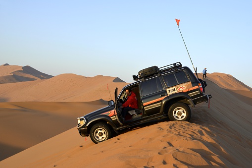 Badain Jaran, China - October 6, 2014: Local driver is ready to start riding his 4x4 jeep on a huge sand dune at dawn in Badain Jaran desert. Badain Jaran is home to some of the tallest stationary dunes on Earth, some reaching a height of more than 500 meters. The desert features over 100 lakes that lie between the dunes, some of which are fresh water while others are extremely saline. 