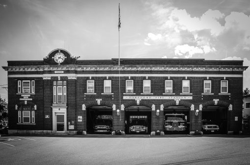 Augusta, USA - June 29, 2014: Facade of the Fire Station in Augusta (Maine), where the four doors are opened and we see the trucks in each door. The building was erected in 1920. Picture taken during daytime in Summer. Black and white image.