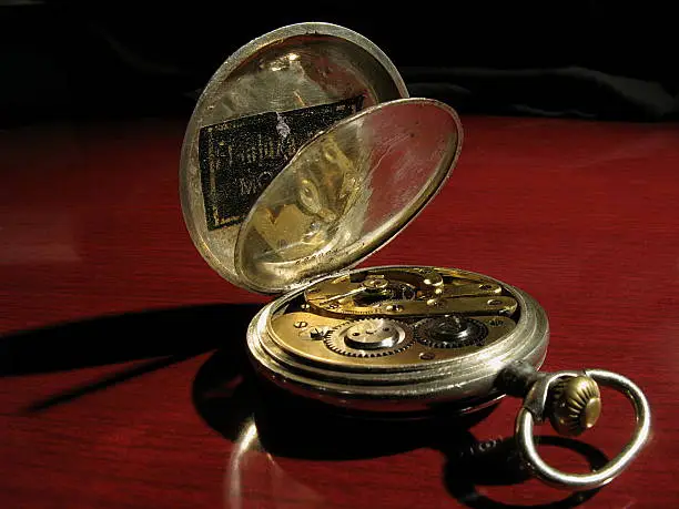 Vintage pocket watch with opened back cover and visible watch mechanism, on red wooden background.