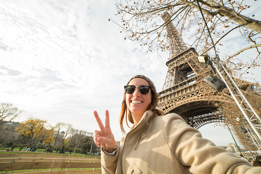 Young cheerful woman near the Eiffel tower in Paris-France takes a selfie portrait using her mobile phone. 