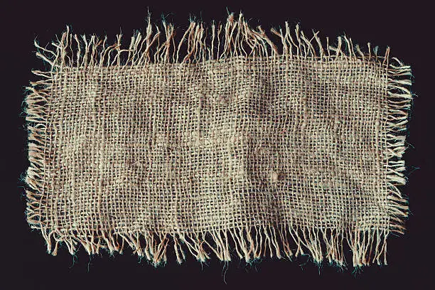 A piece of linen fabric with frayed edges on a black background
