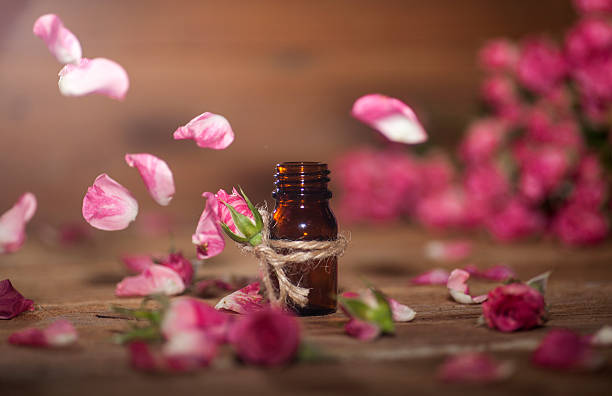 Rose Essential Oil Closeup of bottle with rose essential oil with falling leaves on wooden background. potion bottle retro revival old fashioned stock pictures, royalty-free photos & images