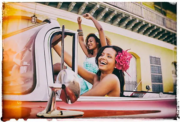 Vintage image of two young caribbean woman in an antique car in Trinidad, Cuba.