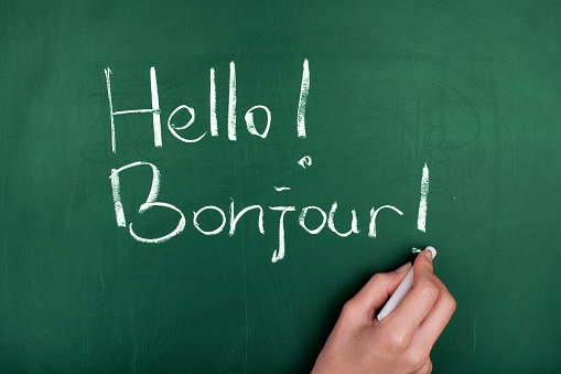 Woman hand writing ' Hello! Bonjour! ' on green blackboard