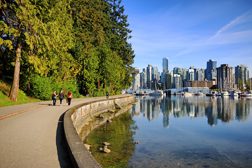 Vancouver, Сanada - April 29, 2014: Stanley Park Seawall Path with pedestrians and cyclist, Vancouver waterfront marina and and modern condonimums and office towers are in the background