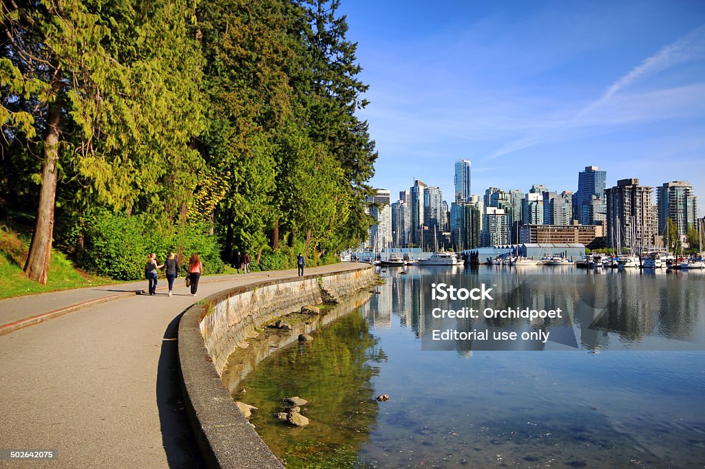 Stanley Park Seawall Path Vancouver, Сanada - April 29, 2014: Stanley Park Seawall Path with pedestrians and cyclist, Vancouver waterfront marina and and modern condonimums and office towers are in the background Stanley Park - Vancouver - Canada Stock Photo