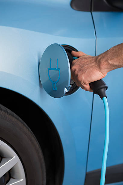Charging of an electric blue car. Close up image of man's hand holding electric cable plug, charging 100% electric blue car with zero emission. two pin plug stock pictures, royalty-free photos & images