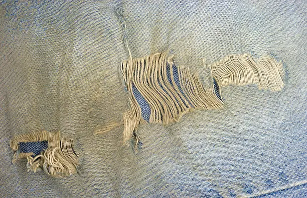 Close view of an old pair of bluejeans that are dirty and worn with frayed holes.