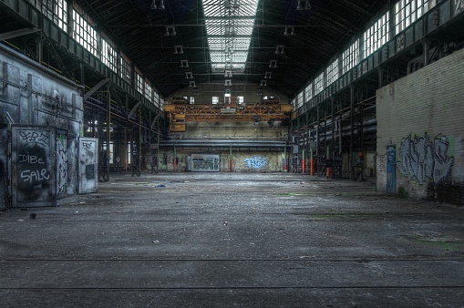 Dark brick facade of an old abandoned factory. The stones are damaged and outdated, but new windows have been installed so that the restored building can be used again.