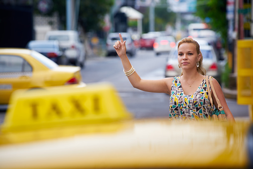 blond businesswoman calling yellow taxi with arm raised in street. Tourism and business travel
