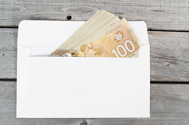 banconote da 100 dollari canadesi in busta bianca su un tavolo di legno - banconota di dollaro canadese foto e immagini stock
