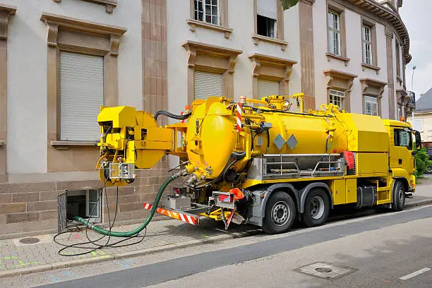 Sewage - sewerage - truck on city street in working process to clean up sewerage overflows, cleaning pipelines and potential pollution issues from an modern building. This type of truck is used for residential septic systems or commercial sewage systems