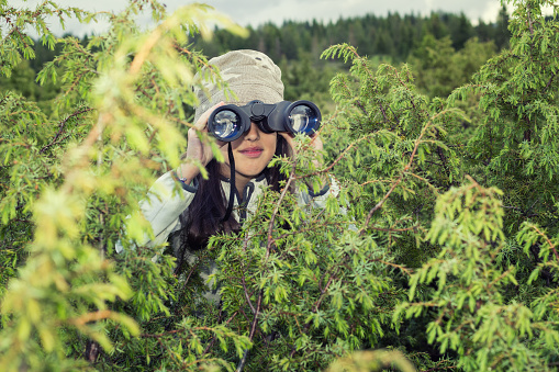 Young man hiker walking in forest using binoculars