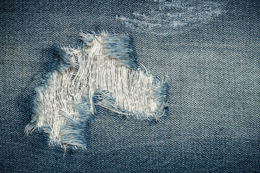 Texture of blue torn denim jean with hole and threads, background