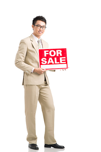Cheerful real estate agent holding for sale signboard
