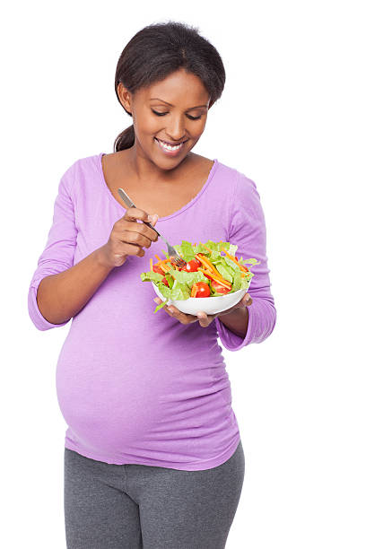 uśmiechnięta kobieta w ciąży jedzenie świeże sałatki. - vegan food cheerful vertical indoors zdjęcia i obrazy z banku zdjęć