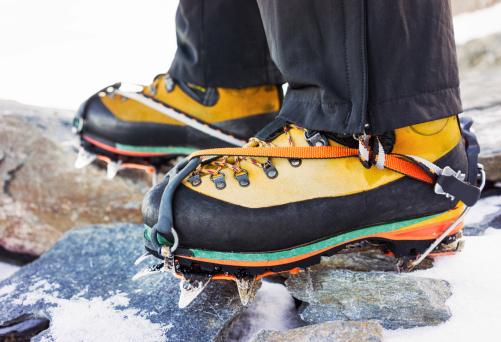 Heavy duty mountaineering boots,with crampons attached. Photographed among snow and rock in the Alps.