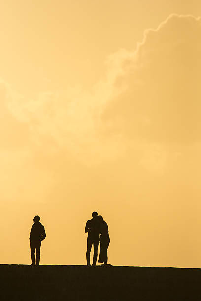Chania, Greece - April 29, 2015: Three people at sunset watching the scenery on the narrow harbour wall separating Chania harbour from the Mediterranean Sea