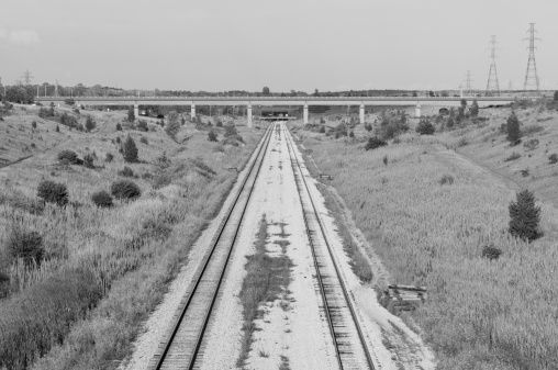 Black and White image of Train Tracks going under a bridge to a tunnel.