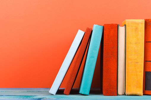Row of colorful hardback books, open book on red background