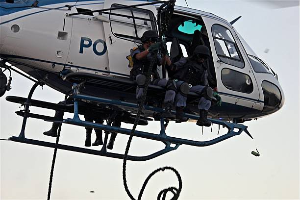 SWAT officers prepare for exit from police helicopter Bergvliet, Cape Town, South Africa - April 4th, 2011: Members of the South African Police Service's Tactical Response Team (a national SWAT unit) begin debussing from a "Squirrel" helicopter from the air-wing. A smoke grenade has been thrown from the helicopter and the other officer deploys the "fast-rope" from which they will descend / abseil to the ground. hand grenade photos stock pictures, royalty-free photos & images