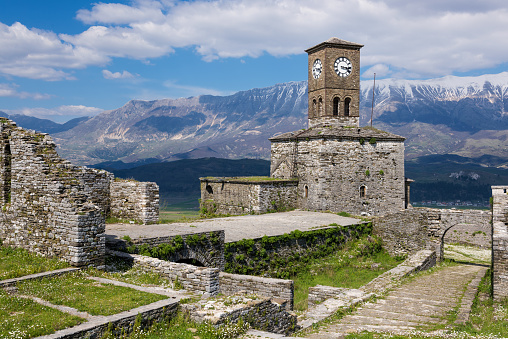 Gjirokaster, Albania - April 9, 2015: The bell tower and part of the castle of the city with snowy surrounding mountains
