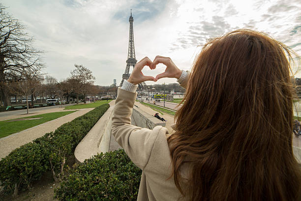 istock Young woman near Eiffel tower makes heart shape finger frame 502730548