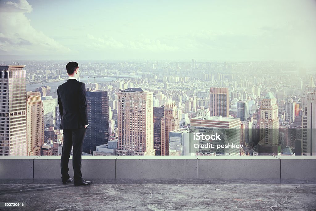 Businessman on the roof and looking at the city Businessman on the roof and looking at the city with skyscrapers Looking Stock Photo