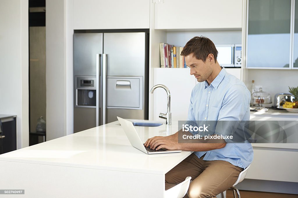 Keeping his blog followers satified Cropped shot of a young man sitting in the kitchen with his laptop 20-29 Years Stock Photo