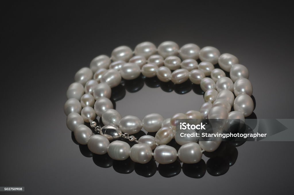 Freshwater pearls Necklace made of freshwater pearls coiled on a black reflective surface. 2015 Stock Photo