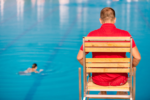 Lifeguard on duty, sitting in lifeguard chair, overlooking pool. Polarizing filter