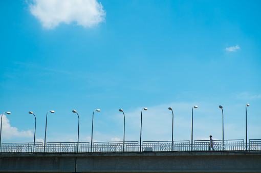 Man walking on footbridge against blue sky