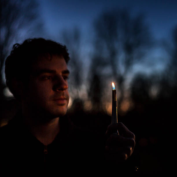 istock Young Man Looking at Flickering Candle Outdoors At Night 502776016