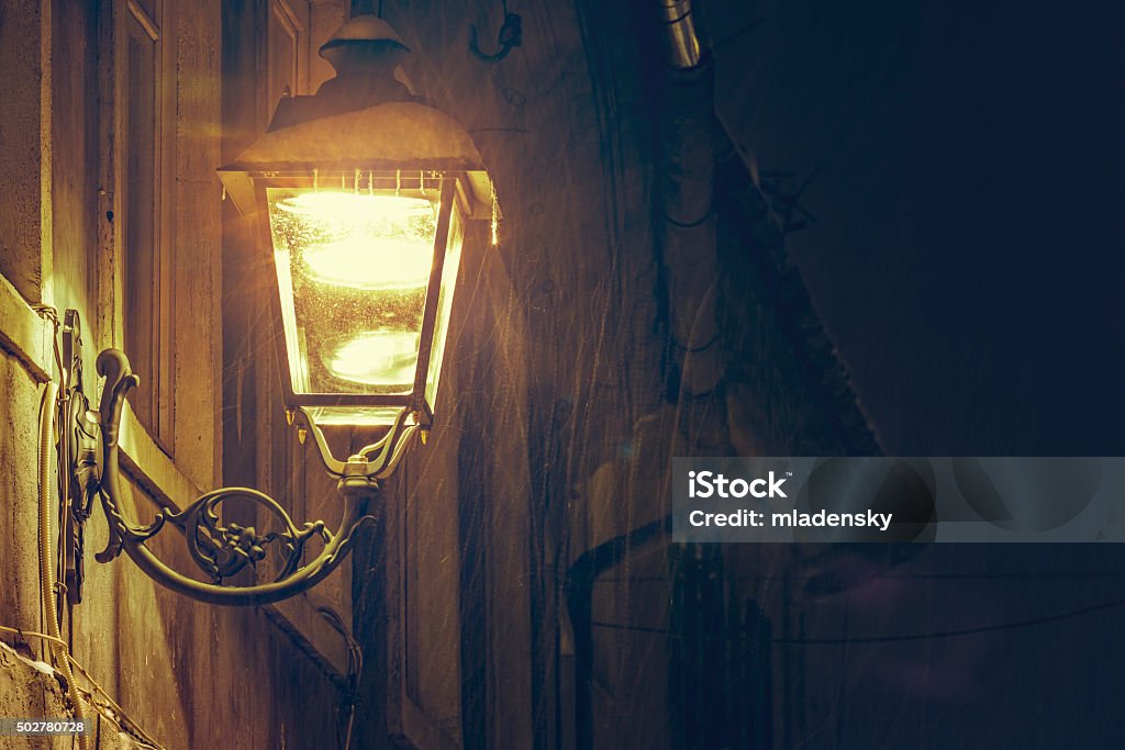 Glowing street lamp Vintage iron street lamp glowing into the night against an old building exterior wall, while snowing. 2015 Stock Photo