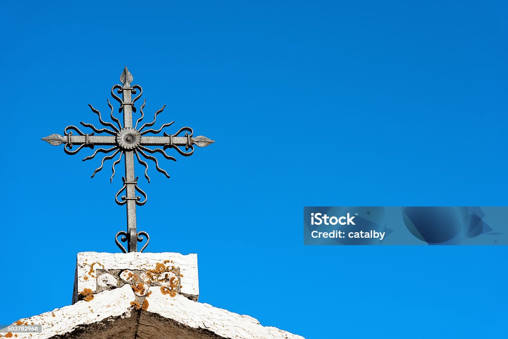 Wrought Iron Cross on Blue Sky Stone roof of church with wrought iron cross against the blue sky 2015 Stock Photo