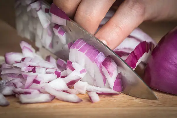 Chef chopping a red onion with a knife on the cutting board