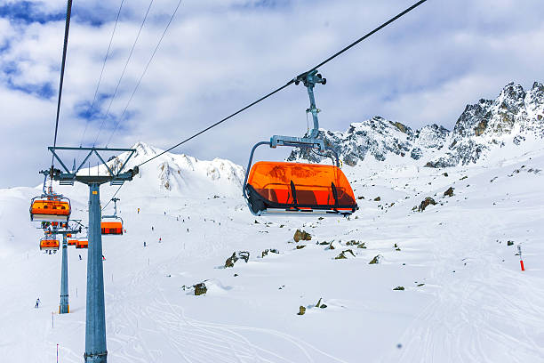 Horizontal image of two ski lift's gondolas with snowy mountains in background