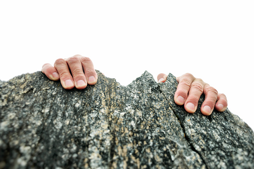 Male hands holding on to the top of a rock cliff, viewed from above. Good for business concepts, struggle, tenacity, conquering adversity, reaching the top, etc, as well as climbing.