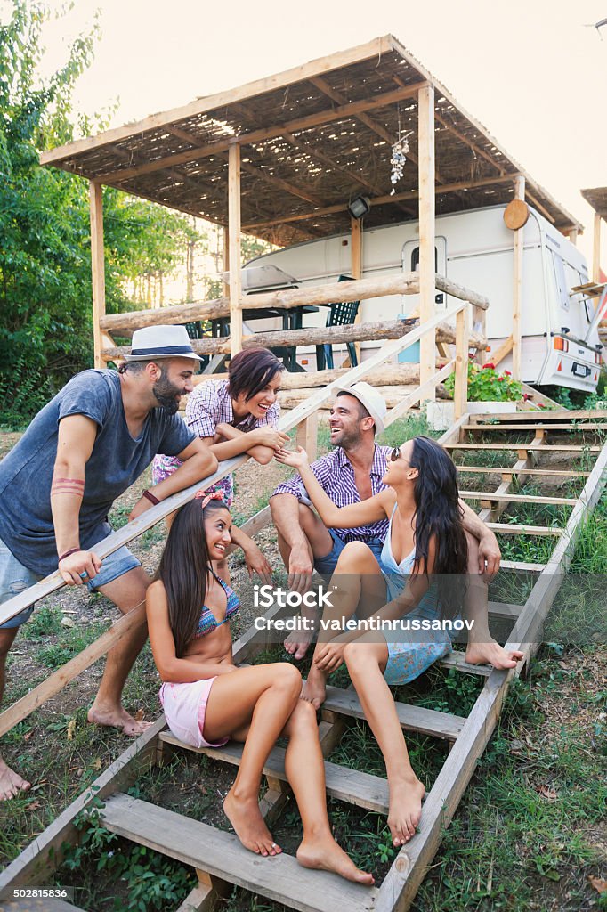 Young people having fun on stairs outdoor Group of young people having fun on stairs, talking and laughing. Wear hats and shorts, dresses and swimsuits. As background is a caravan. 2015 Stock Photo