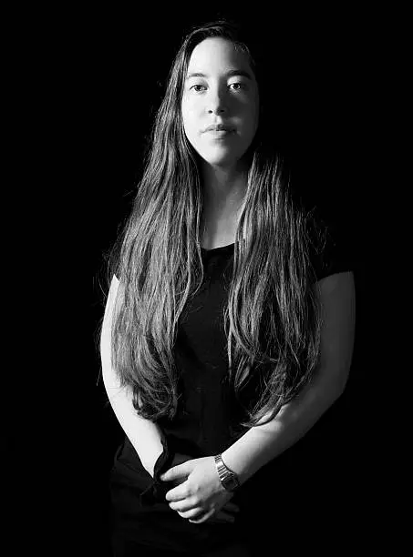 Dramatic low-key Rembrandt lighting portrait of an 18 year old young woman with long hair on black background in black and white (B&W)