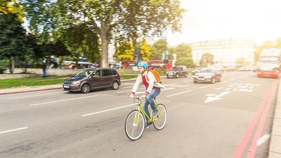 Hipster man cycling in London on a busy street. He is riding a fixed gear bike and wearing a helmet. Panning technique to blur cars and background. Transportation and lifestyle concepts.