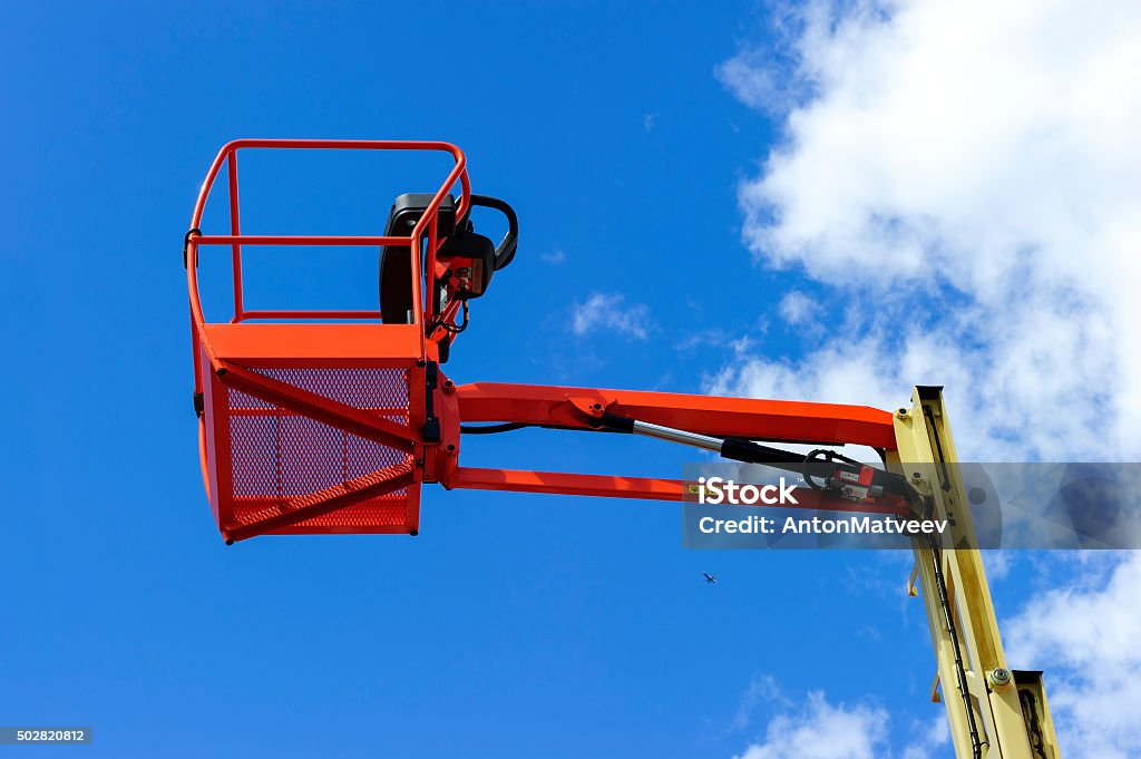 Hydraulic lift platform Hydraulic lift platform with bucket of construction vehicle painted in orange and beige colors with white clouds and blue sky on background  Basket Stock Photo